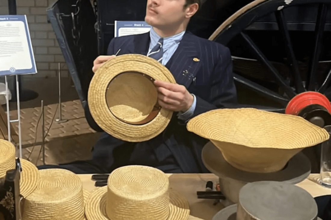 Young man sat behind a table holding a straw hat