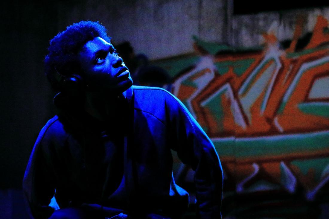Male sat in blue light in from of graffiti wall