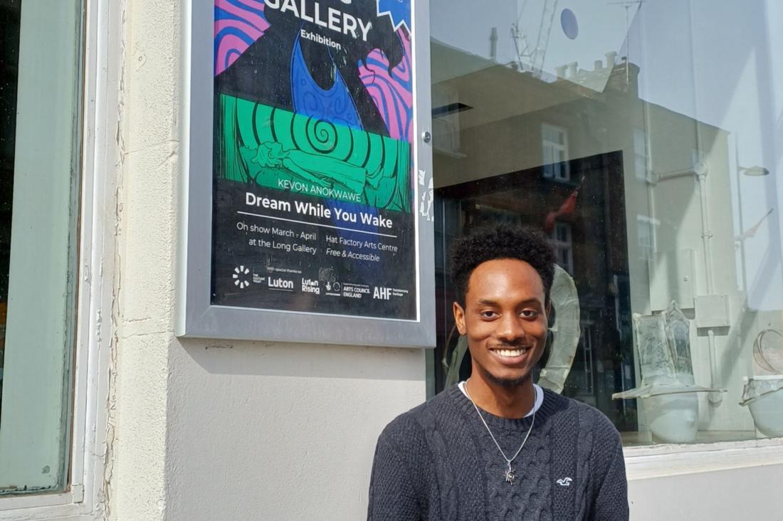 Kevon standing in front of his art outside, in front of the Hat Factory Arts Centre