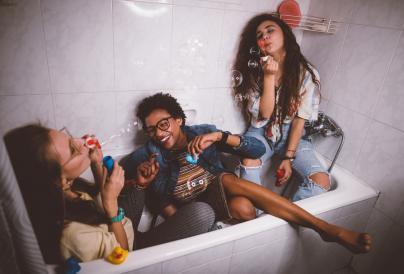 3 girls sitting in a bath blowing bubbles and laughing.